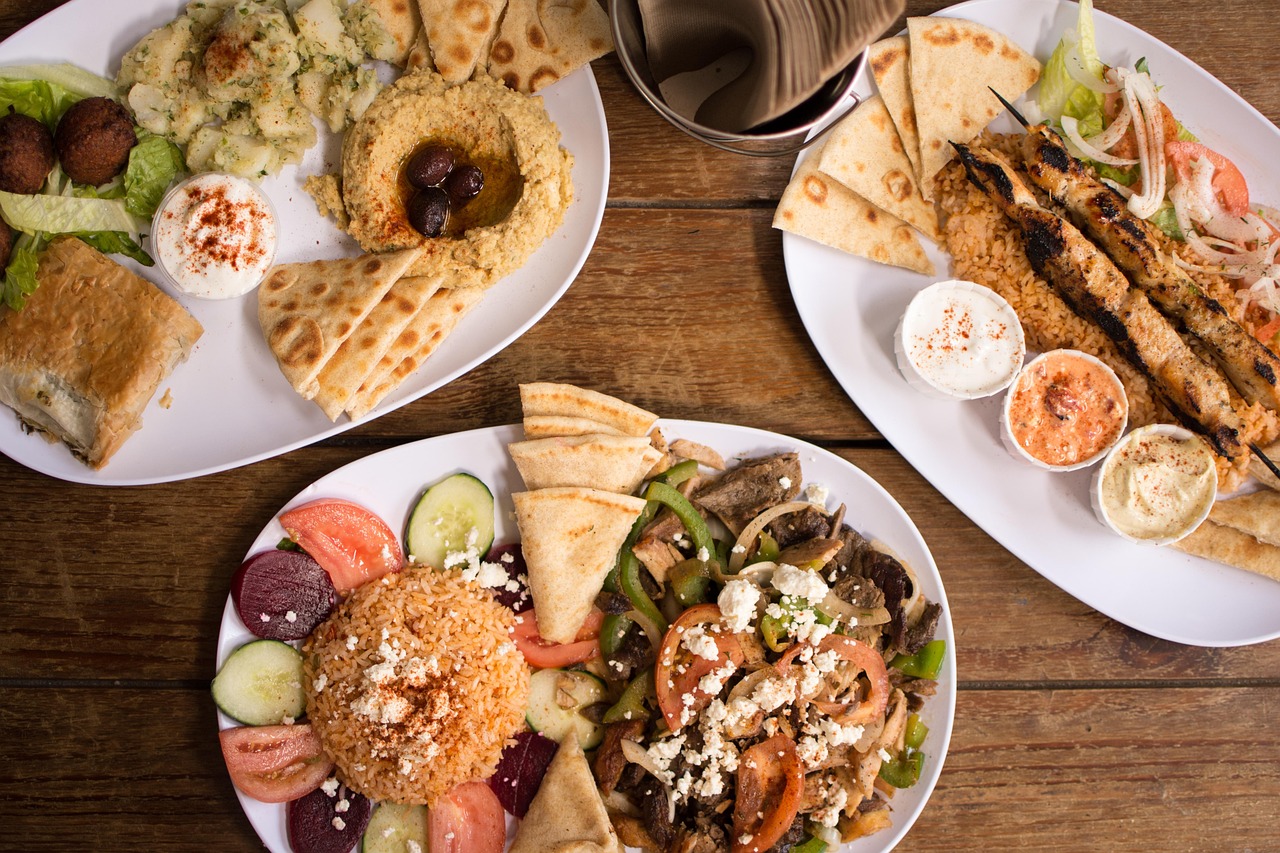 Greek plates on a wooden table: falafel, hummus with olives, souvlaki over rice, pita and dips